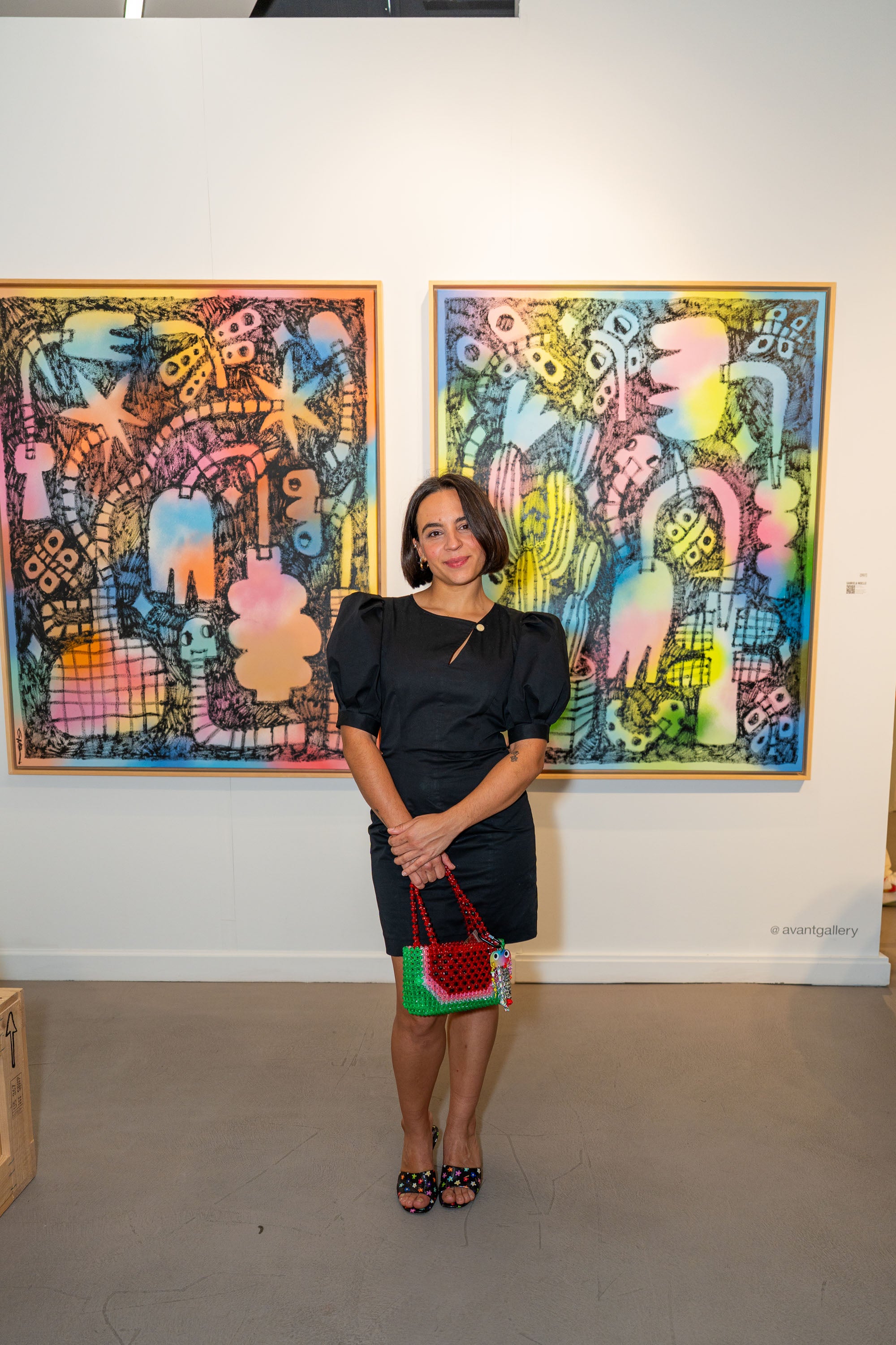 A photo of Gabriela Noelle posing in front of two of her paintings at Avant Gallery Miami each. 